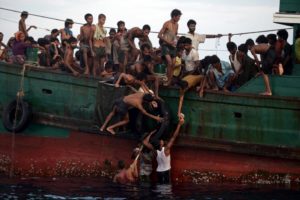 Several Rohingya men pass food supplies dropped by a helicopter to others aboard a boat drifting in Thai waters in the Andaman Sea on May 14, 2015. © UNHCR/Christophe Archambault