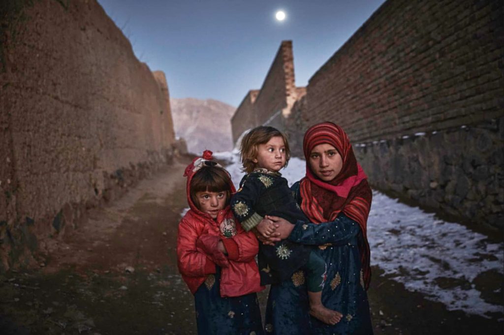 3 children standing in a a dirt-road alleyway.