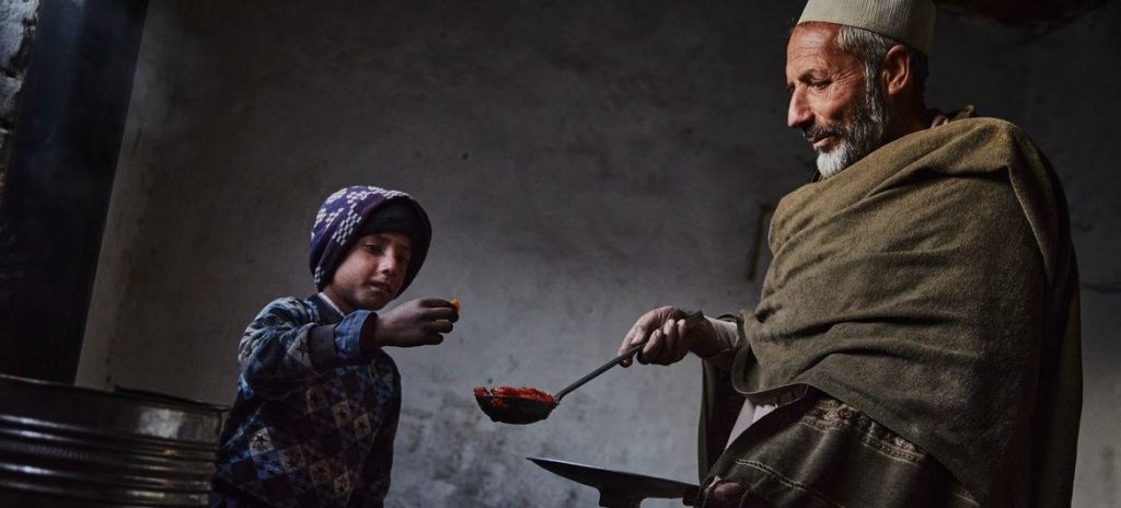 A man serves a ladle of soup to a child.