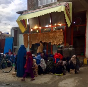 Women sitting and standing outside a bakery at dusk in Kabul, Afghanist. Photo credits: Sonia Cautain.