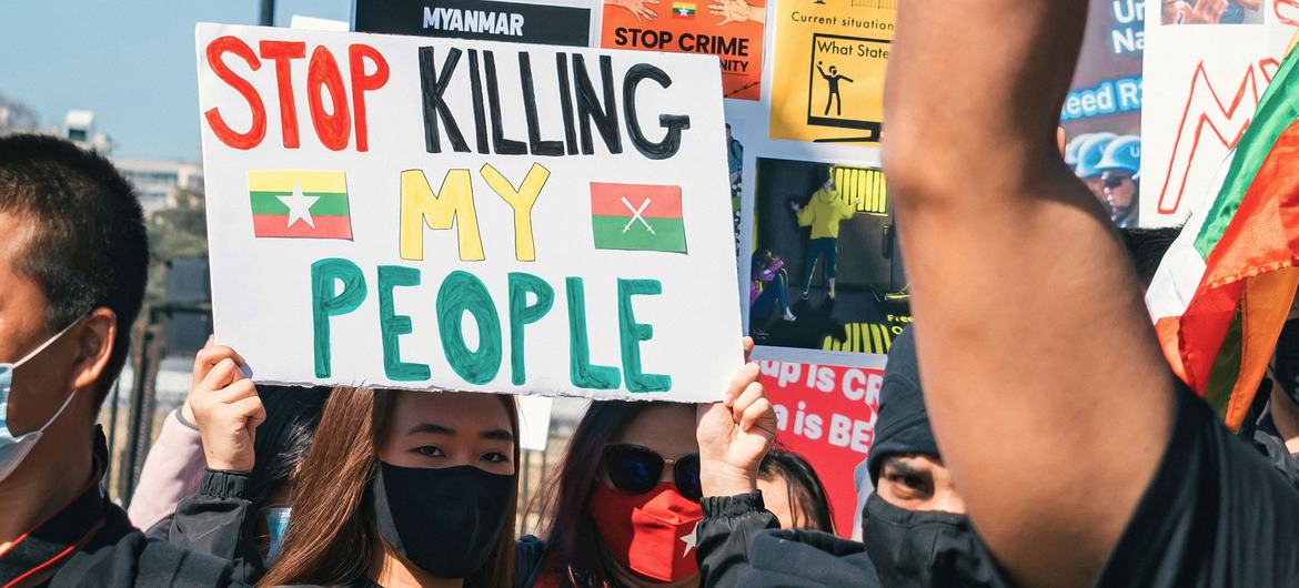 Someone wearing a face-mask holds up a sign which says "Stop Killing My People" in a group of other people also holding placards.
