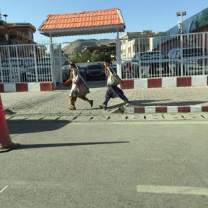 Two young men walk on a side walk in Kabul, with big cloth bags under on their backs.